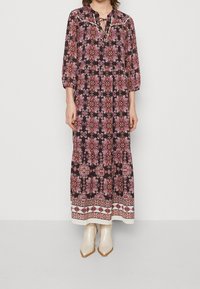 Robe maxi en tissu sombre avec des motifs floraux en rose et blanc. Elle possède des manches trois quarts, un décolleté à nouer et un ourlet contrastant.