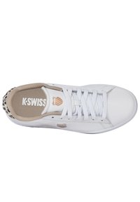 Baskets de sport blanches avec un upper en cuir lisse, des bords texturés beiges et un talon à motifs. Comprend des lacets blancs et un logo sur le côté.