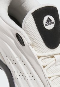 Vit sneaker med överdel i mesh, texturerade läderdetaljer, svart logotyppatch och perforerade detaljer längs sidan.