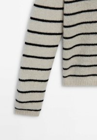 Manche de pull crème en tricot avec des rayures horizontales noires régulièrement espacées et un poignet côtelé sur fond blanc.