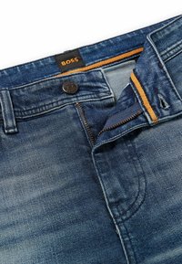 Jeans de mezclilla en un lavado azul oscuro con una textura desvaída. Cuentan con cierre de botón y cremallera, con un contraste en amarillo dentro de la cinturilla.