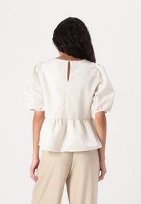 Valge puff-sleeve top peplum alläärega, peene tekstuurilise mustriga ja avausega seljaosas. Stiilitud beežide laiade pükste juurde.