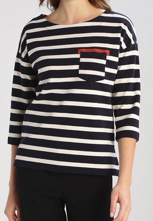Top a maniche lunghe a righe blu navy e crema con una tasca frontale accentata in rosso e scollo a barca. Tessuto morbido con vestibilità comoda.