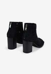 Botas de tobillo de ante negro con un diseño texturizado, detalles recortados y cremalleras laterales. Cuentan con un tacón grueso negro para mayor estabilidad.