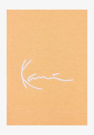 Kollane puuvillane T-särk, millel on valge tikitud tekst; pehme tekstuur ja sile viimistlus ning nähtavad õmblused äärel.