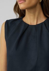 Marinekleurig mouwloos top met een geplooide halslijn en een gladde textuur, met een gestructureerd en minimalistisch ontwerp zonder versieringen.