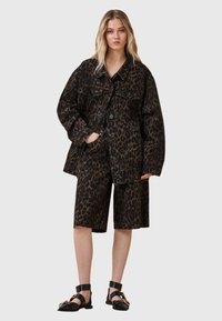 Ensemble composé d'une veste et d'un short en tissu texturé imprimé léopard. Présente une silhouette oversized, de grandes poches et des détails de boutons. Des chaussures noires complètent le look.