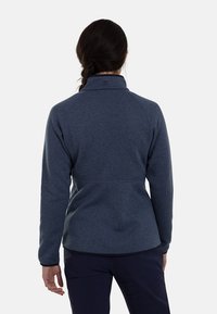 Donkerblauwe fleecejas met een hoge kraag, gestructureerde stof en een getailleerd ontwerp. Heeft een subtiel patroon en contrasterende stikseldetails.