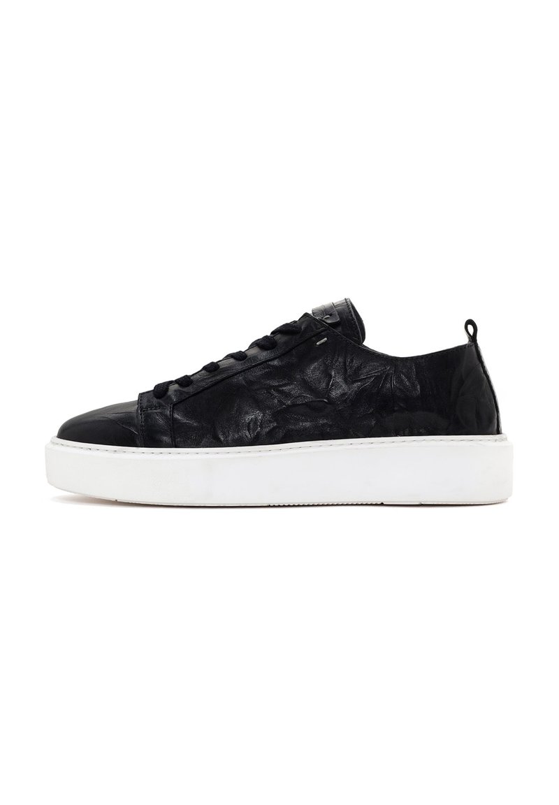 Black leather sneaker with a wrinkled texture, round toe, black laces, and white rubber sole. Features a small loop at the heel.