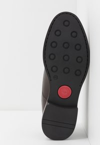 Semelle d'une chaussure habillée en cuir avec des crampons circulaires et un logo circulaire rouge près de l'arche, taille marquée 41 sur la semelle.