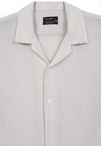 Camicia tessuta leggera beige chiaro, con una vestibilità rilassata. Presenta un colletto standard e cinque bottoni sul davanti. Etichetta: Calliope, taglia L.