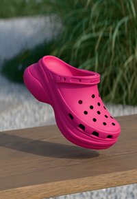 Rosa formet klog i syntetisk materiale, med ventilasjonsåpninger og stropp. Jevn tekstur med lett glans på en treoverflate.