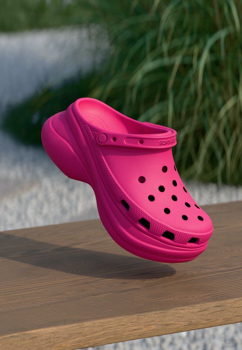 Rosa formet klog i syntetisk materiale, med ventilasjonsåpninger og stropp. Jevn tekstur med lett glans på en treoverflate.