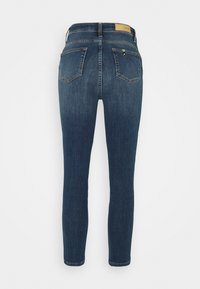 Jeans ajustados en denim azul oscuro, con cintura media, diseño de cinco bolsillos y un parche de cuero color marrón en la parte posterior de la cintura.