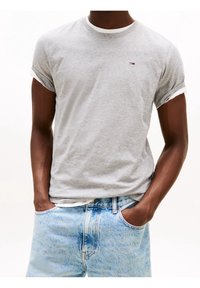 Gray cotton t-shirt with rolled short sleeves, featuring a small logo on the chest and layered with a white crew neck. Worn with light blue jeans.