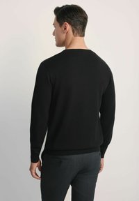 Czarny sweter z dzianiny, z długimi rękawami, okrągłym dekoltem i ściągaczami na rękawach. Połączony z ciemnoszarymi, teksturowanymi spodniami. Gładki materiał.