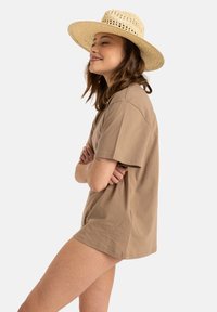 Světlé hnědé, oversized bavlněné tričko s krátkým rukávem, doplněné širokým tkaným slaměným kloboukem. Jednoduchý, uvolněný design.