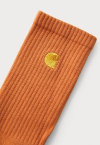 Orange ribbede sokker med et lille gult spiral-logo broderet nær toppen. Lavet af blødt, struktureret stof.