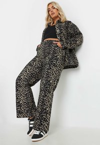 Chaqueta y pantalones de estampado de leopardo en beige y negro, con un ajuste relajado y bolsillos laterales, combinados con zapatillas negras con detalles blancos.
