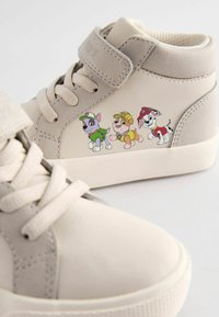 Baskets montantes beiges avec une texture douce, dotées d'une sangle Velcro et d'un motif imprimé de chiots en cartoon sur le côté extérieur.