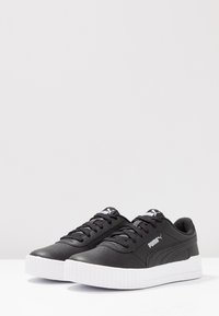 Black leather sneakers with a white rubber sole, round toe, flat laces, and branded logo on the side and tongue.