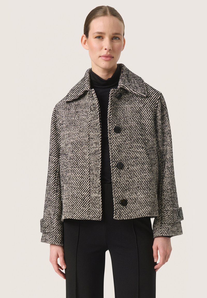 Zwart-witte houndstooth cropped jack met grote kraag, dubbelknopen en manchetdetails. Gemaakt van een gestructureerde stof.