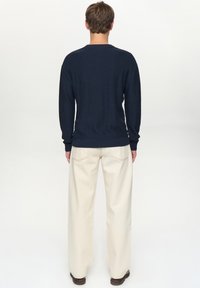 Marineblauwe trui met lange mouwen, geribbelde zoom en ronde hals, gecombineerd met roomkleurige broek met wijde pijpen en subtiele stikdetails.