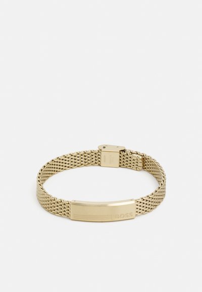 Bracelet en maille dorée avec une plaque plate gravée du mot "BOSS". Le design est élégant avec une texture métallique et un fermoir sécurisé.