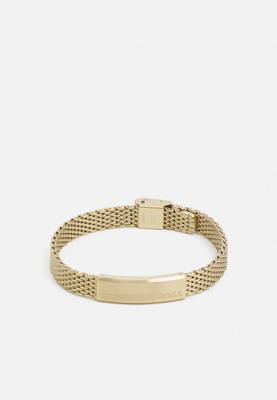 Bracelet en maille dorée avec une plaque plate gravée du mot "BOSS". Le design est élégant avec une texture métallique et un fermoir sécurisé.