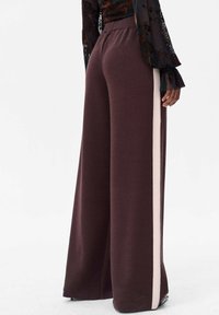 Brede broek in donkerbruine tricotstof met een contrasterende lichtroze zijstreep, voorzien van een elastische tailleband en een zachte textuur.
