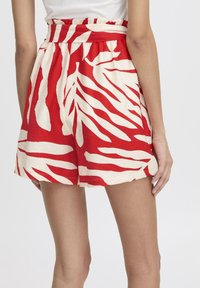 Shorts rouges et blancs avec un motif audacieux de feuilles, dotés d'une taille ajustée et d'une coupe ample, fabriqués en tissu léger.