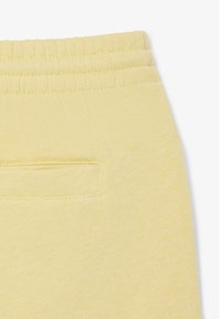 Pantaloni della tuta di un giallo chiaro, in tessuto morbido, con vita elastica e una piccola tasca cucita sulla parte posteriore.