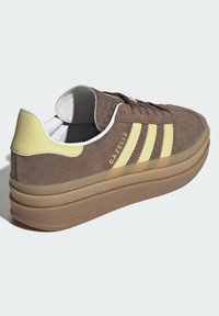Brune suedesneakers med gule detaljer, med tre gule striper, rund tå, og lagdelt gummisåle med preget merke.