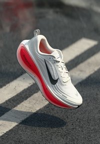 Baskets de course Nike blanches avec un swoosh noir, une semelle rouge, une tige texturée et un design superposé, présentant la marque "zoomX" sur le côté.
