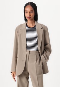 Overdimensjonert beige blazer med notched lapels, kombinert med en marineblå og hvit stripet t-skjorte, og tilpassede bukser, som skaper et monokromatisk utseende.