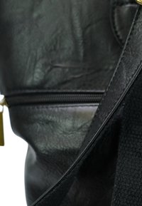 Zwarte leren tas met een textuur oppervlak, voorzien van een ritsluiting en een geweven zwarte schouderriem. Vergezeld van een gouden hardwaredetail.