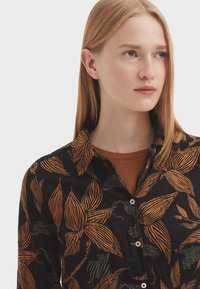 Black shirt featuring a floral pattern in orange and green. The design includes a button-up front and a collar, with a textured fabric finish.