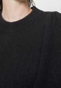 Svart stickad tröja med rund hals, med en mjuk textur och subtila puffärmar. Tyget verkar mysigt och varmt.