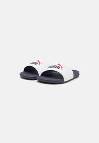 Puma Slide-Sandalen mit einem weißen synthetischen Obermaterial und einer navyfarbenen Gummisohle. Mit rotem Logo-Detail und offener Zehenpartie.