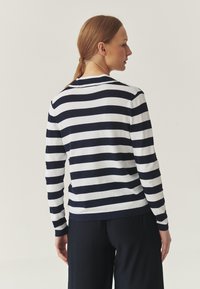 Navy ja valge triibuline pikako sleeves top ümmarguse kaelusega ja soonikute allservaga, kombineeritud tumedate laiade pükstega. Sile tekstuur.