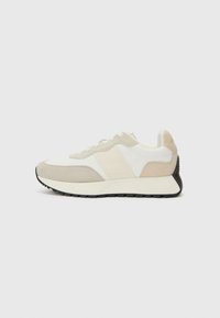 Sneaker beige e bianche con un design di materiali misti che include camoscio e tessuto, con una suola nera testurizzata e accenti minimalisti.
