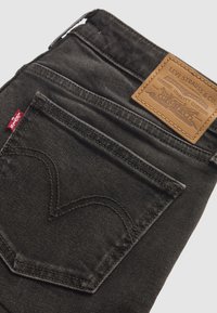 Σκούρα γκρι τζιν Levi's διπλωμένα, εμφανίζοντας την πίσω τσέπη με το κόκκινο ταμπελάκι και την καφέ δερμάτινη ετικέτα της μάρκας Levi Strauss & Co. πάνω από τη μέση.