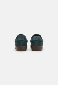 Green suede sneakers with a low profile design, featuring brown rubber soles and a textured finish on the upper for grip and comfort.