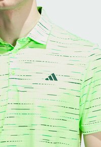 Polo de color verde claro con un patrón texturizado y rayas horizontales. Logo de Adidas bordado en negro en la parte superior izquierda. Mangas cortas.