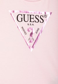 Pink T-shirt featuring a metallic triangle logo with "GUESS U.S.A." and the words "WASHED JEANS" in black, with a prominent question mark.