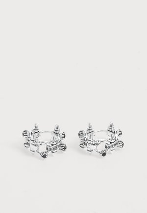 Paire de boucles d'oreilles anneaux argentées avec des détails en pointe et perles disposés uniformément autour des anneaux sur fond blanc.