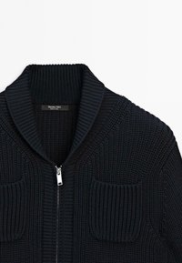 Cardigan noir en tricot avec fermeture éclair à l'avant, col châle côtelé et deux poches carrées sur la poitrine, présenté sur fond blanc.