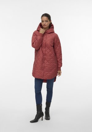 Vadderad röd jacka med huva, tryckknappsförsedd framtill, sidofickor och långa ärmar. Kombinerad med blå jeans och svarta ankelboots.