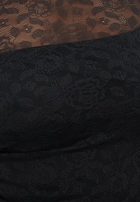 Μαύρο υφασμάτινο δαντέλα με λουλούδια καλύπτει γυμνό δέρμα, δημιουργώντας ένα διαφανές σχέδιο από τριαντάφυλλα και φύλλα στην περιοχή του στήθους και των ώμων.