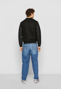 Sort bomberjakke med læderærmer, kombineret med lyseblå jeans. Jakken har en ribbet krave og manchetter, samt en afslappet pasform.